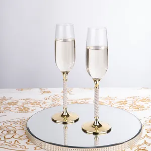 Calici da champagne dorati con steli incrostati di cristalli su vassoio a specchio.