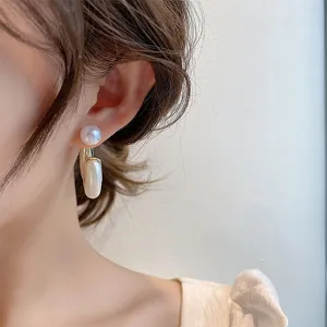Detail view of elegant gold-toned drop earrings featuring round and oblong pearls
