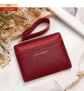 Detalle de monedero corto rojo para mujer con correa y texto dorado grabado.