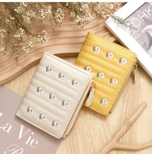 Close-up of floral embroidered short wallets in beige and yellow on a wooden tray.