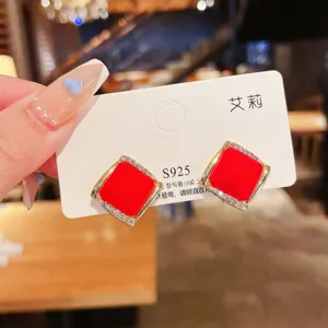 Close-up of elegant red matte square stud earrings with rhinestone borders on silver needle.