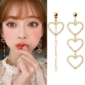 Elegant heart-shaped gold drop earrings with rhinestone accents and faux pearls on model