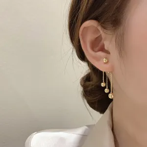 Close-up detail of elegant golden tassel drop earrings with solid beads on a model's ear