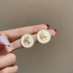 Close-up of gold coin earrings featuring a white enamel classical bust relief design