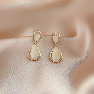 Elegant gold-tone drop earrings featuring milky white cat-eye stones on soft pink silk