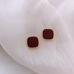 Detailed macro view of minimalist square stud earrings with dark red finish and gold border.
