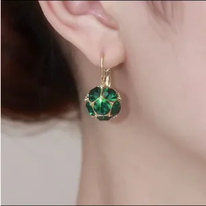 Close-up of elegant gold earrings with faceted green crystal sphere