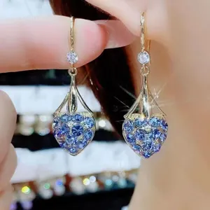 Dettaglio ravvicinato degli orecchini a cuore con cristalli blu e ganci dorati.