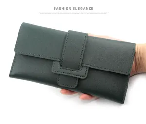 Detailed macro view of a dark green long trifold wallet with buckle held in a hand