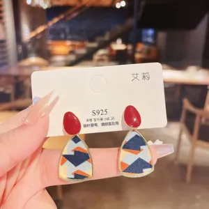 Detailed view of geometric drop earrings featuring patterned fabric and vibrant red stud