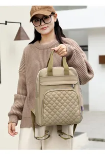 Close-up of beige quilted diaper backpack being held by a model in a casual brown sweater