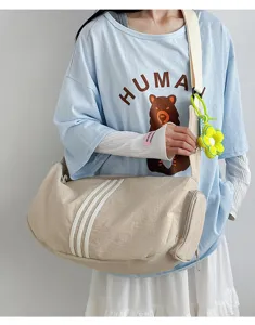 Leichte beige Sporttasche mit drei Streifen und gelbem Blumenanhänger am Model