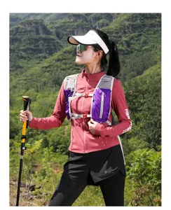 Female model wearing a purple trail running vest backpack in a mountain setting