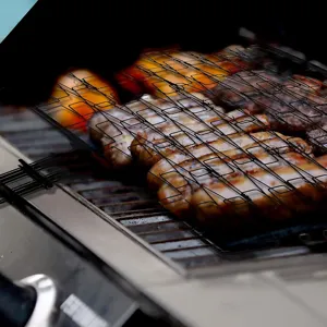 Non-stick rectangular portable BBQ grill basket holding grilled steaks over a fire