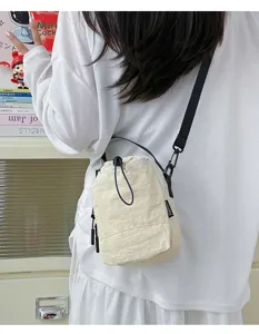 Close-up of lightweight cream nylon crossbody bag worn on shoulder for outdoors.