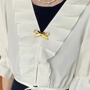 Nahaufnahme einer minimalistischen goldenen 3D-Brosche in Schleifenform auf weißer Bluse