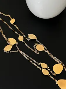 Detailed view of elegant gold brushed metal plate long necklace on textured black background