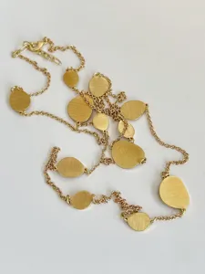 Detailed view showing brushed gold discs on a long chain necklace against white background