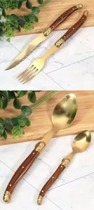 Dettaglio del set di posate Laguiole dorate con manici effetto legno su fondo marmo.