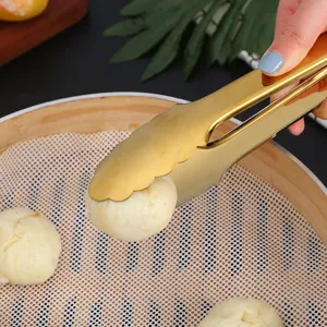 Close-up of gold stainless steel food tongs picking up a bun in a bamboo steamer basket.