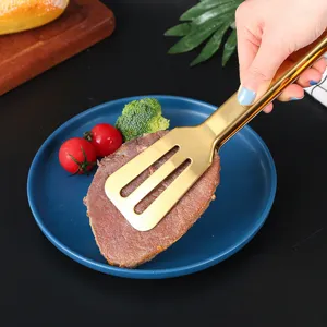 Golden stainless steel food tongs lifting a steak from a blue plate in a kitchen setting