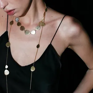 Close-up of elegant brushed gold disc long necklace on model in black silk dress