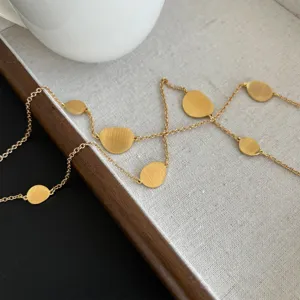 Detailed view of a long gold necklace featuring brushed metal plates on vintage linen.
