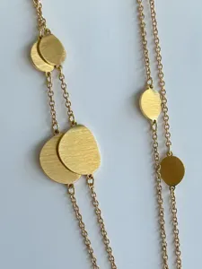 Macro view of brushed gold irregular disc charms on a minimalist long chain necklace