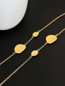 Detailed macro view of an elegant gold long necklace with brushed oval metal plates.