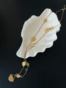 Elegant brushed gold disc long necklace draped over a white shell-shaped jewelry dish.