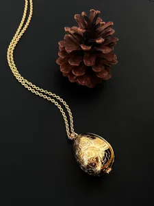 Detailansicht eines goldenen Eianhängers im Vintage-Stil mit feinen Blumenmustern.