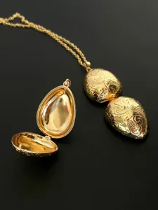 Detailansicht einer goldenen Medaillon-Halskette in Eiform mit gravierten Retromustern.
