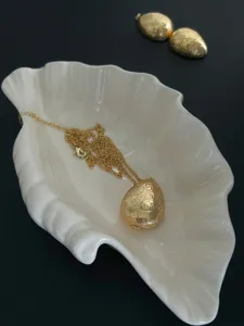 Detailansicht des goldenen Medaillons in Eiform mit Gravur auf einer Muschelschale.