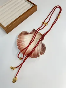 Detail of a French retro long necklace with red beads and gold trumpet charms on a shell.