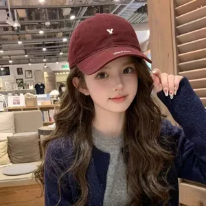 Close-up detail shot of the burgundy baseball cap featuring chic embroidery worn by model.