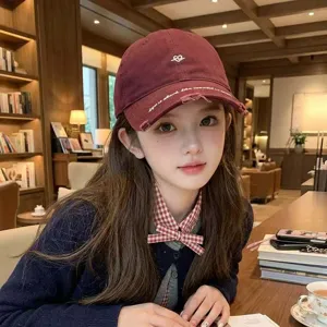 Lifestyle detail of a woman wearing a burgundy embroidered cap in a warm library setting