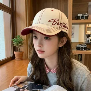 Detailed view of the stylish beige and dark red baseball cap with side embroidery in cozy setting.
