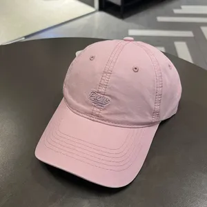 Dettaglio di un berretto da baseball rosa lavato con ricamo viola 'Pious' sul davanti.