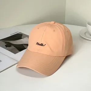 Nahaufnahme einer pfirsichfarbenen Baseballkappe mit schwarzer 'Hello!' Stickerei.