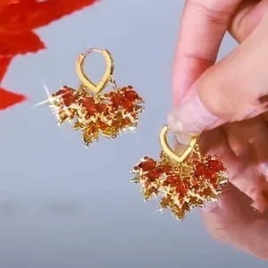 Close-up of elegant gold hoop earrings with sparkling red rhinestone maple leaves