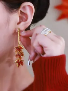 Detailed view of elegant gold-tone maple leaf earrings with red crystals on model