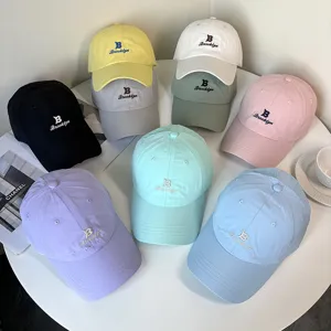 Collection of pastel embroidered baseball caps displayed on a minimalist white table.
