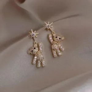 Exquisite close-up of sparkling gold teddy bear drop earrings with star studs on satin