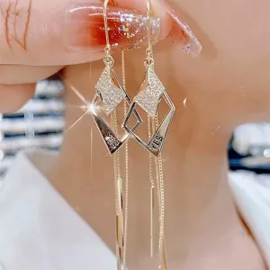 Close-up of geometric rhombus tassel earrings featuring engraved 'YES' and sparkling crystals