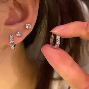 Close-up view of silver-colored mini hoop and stud earrings with sparkling clear stones