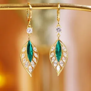 Close-up detail of vintage gold leaf earrings with marquise green and clear gemstones