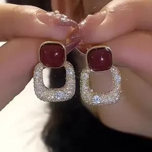 Vue détaillée des boucles d'oreilles dorées avec pierres rouges et pavé de cristaux.