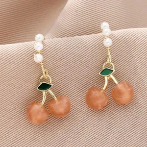 Gros plan détaillé de boucles d'oreilles cerises dorées avec perles et feuilles vertes.