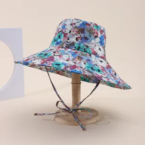 Detailed view of a wide-brimmed floral sun hat with a chin strap on a wooden stand