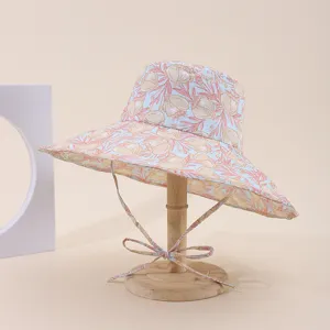 Side view of floral print wide brim sun hat on a wooden stand, soft beige background.